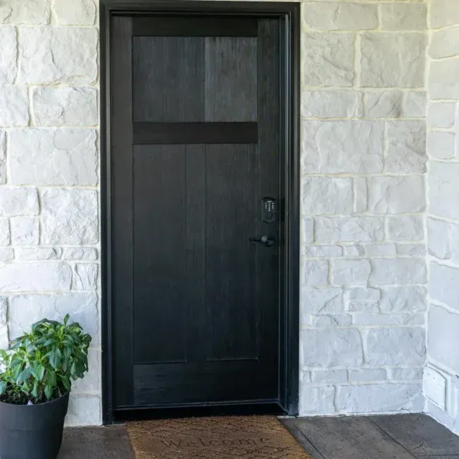 A black door is sitting in front of a white brick wall.