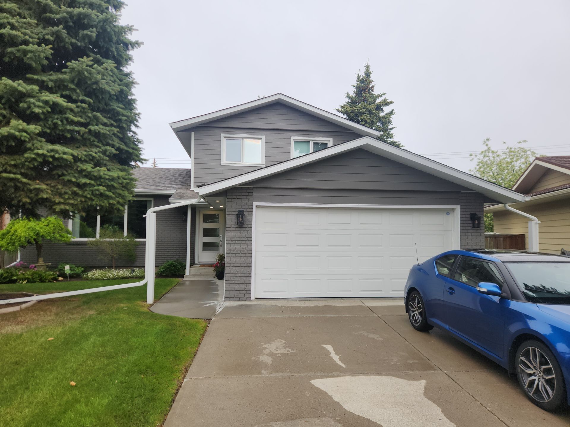 A blue car is parked in front of a house with a garage door.