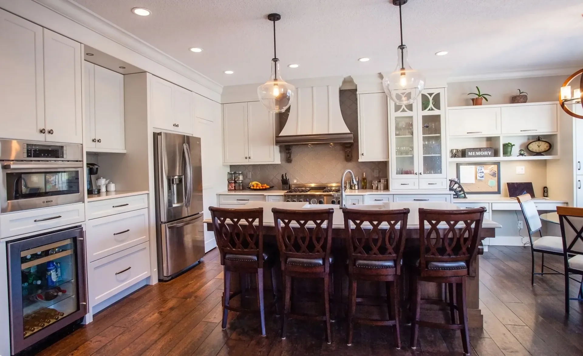 A kitchen with white cabinets , stainless steel appliances , a large island with a table and chairs.