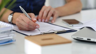 A woman is writing on a clipboard with a pen.