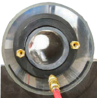 Close-up of a machine component with a silver hemisphere, black ring, and brass fittings. A red hose is attached.