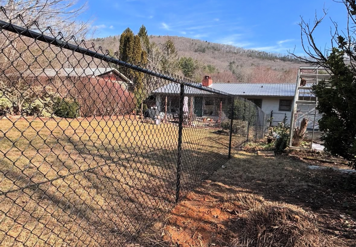 Black chain-link fence in foreground; house and mountain in background on a sunny day.