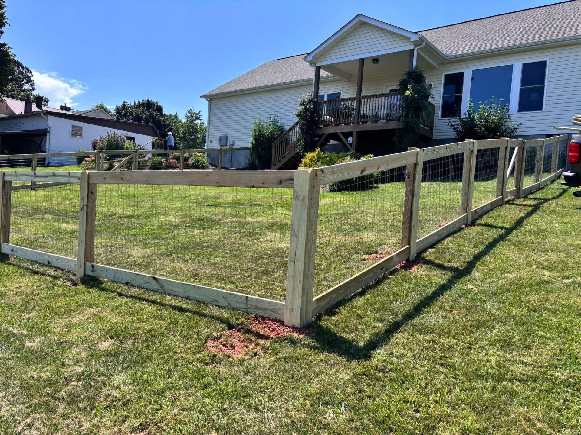 Wooden framed fence with wire mesh on a grassy lawn in front of a house.