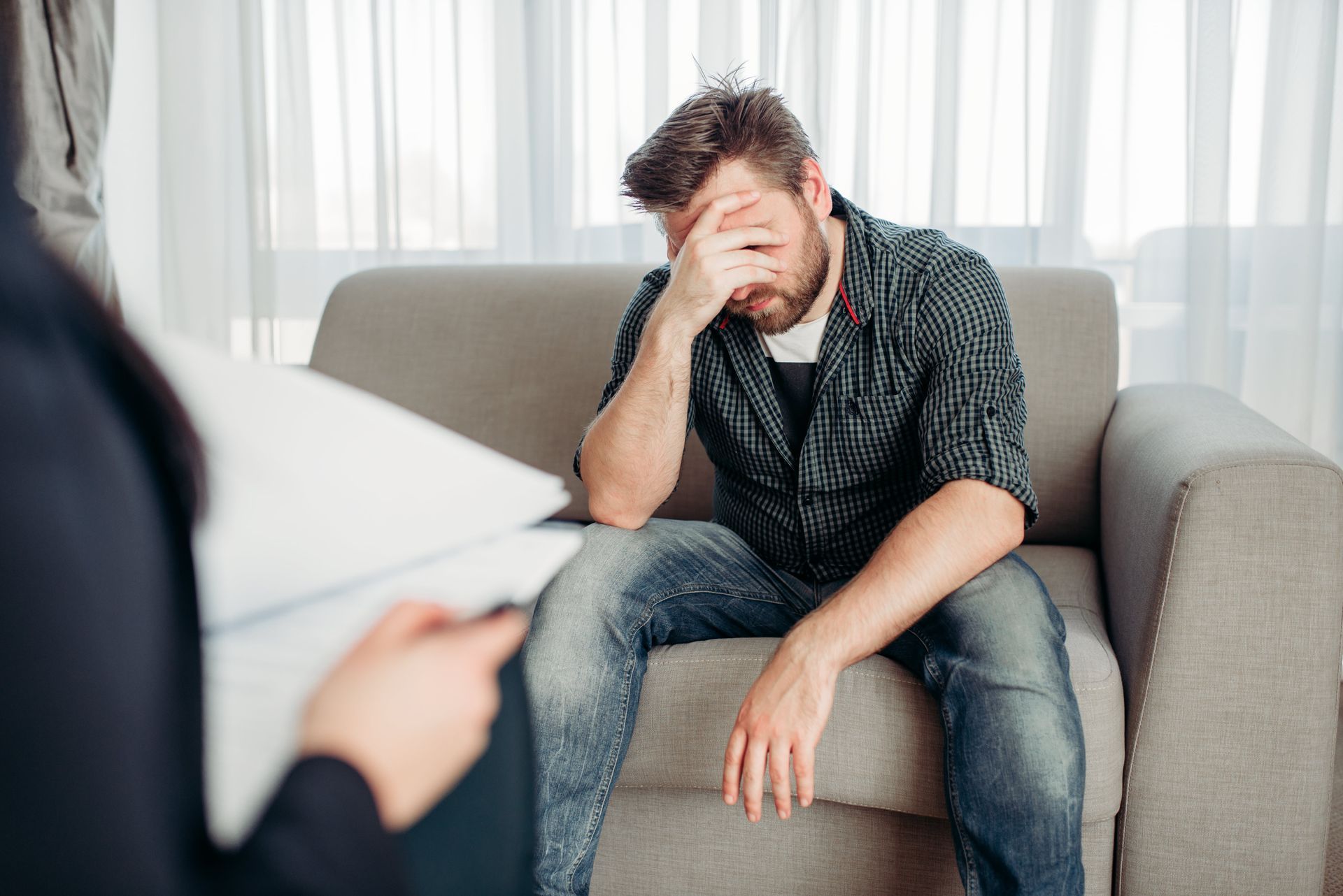 A doctor is writing on a clipboard while a patient sits at a table with their hands folded.