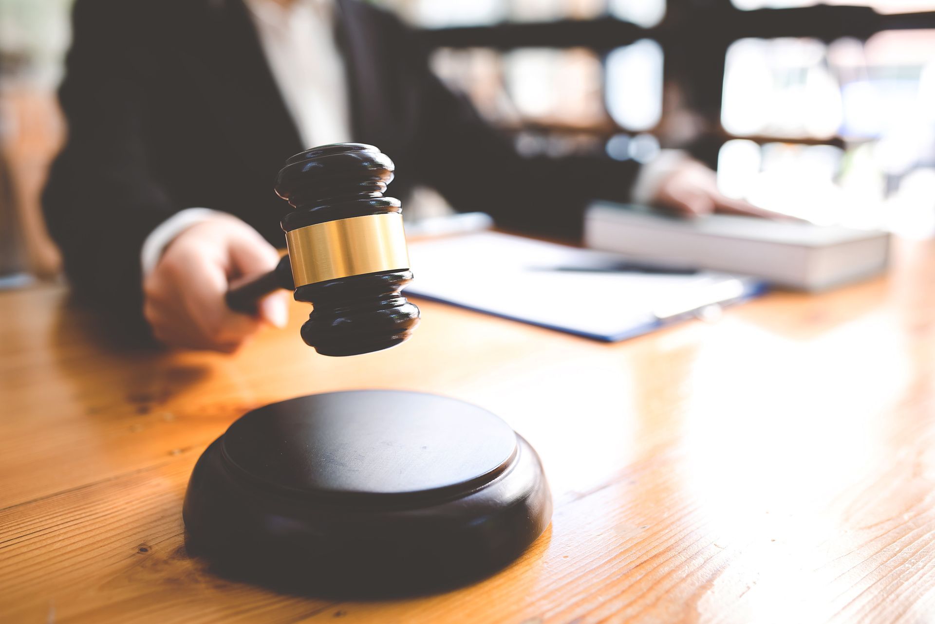 A person in a suit holds a gavel over a wooden block, desk, and legal documents.