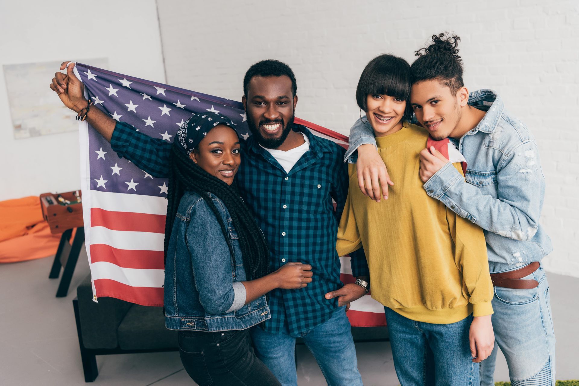 Group of four diverse young people smiling, holding American flag.