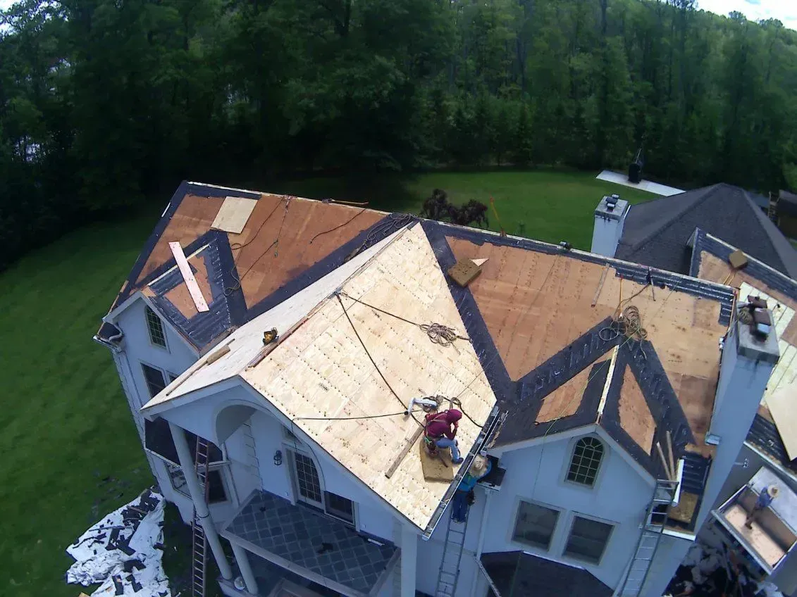 Roofers working on a house roof. Green grass and trees in the background.