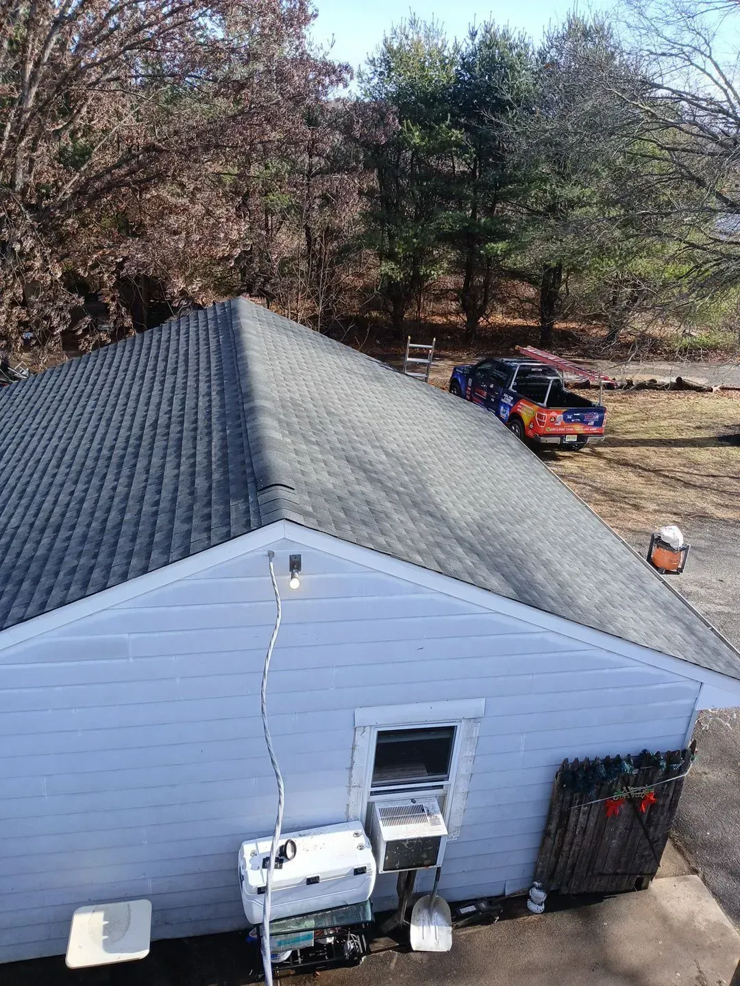 A blue building with a gray roof. A truck is parked nearby, with trees in the background.