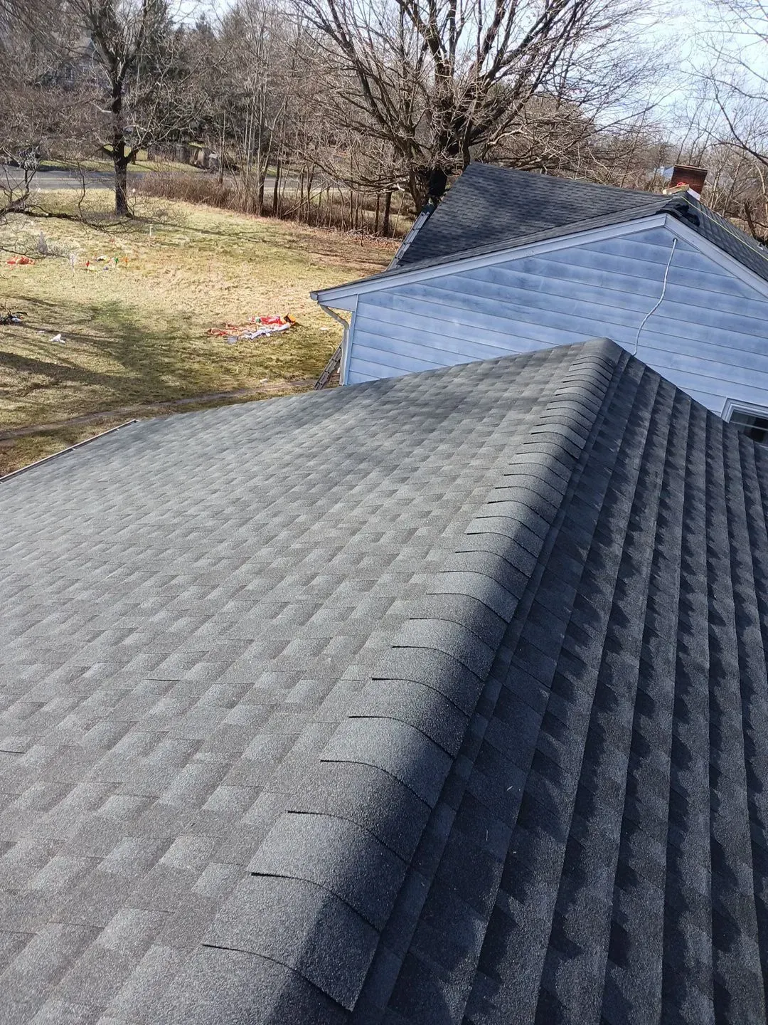 Dark gray asphalt shingle roof on a house, angled view, sunny day.