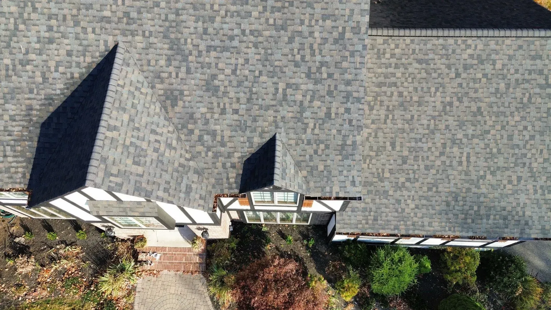 Overhead view of a house with a gray shingled roof, trees, and landscaping.