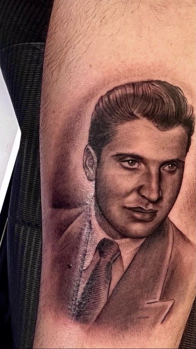 A man has a tattoo of a man in a suit and tie on his arm.