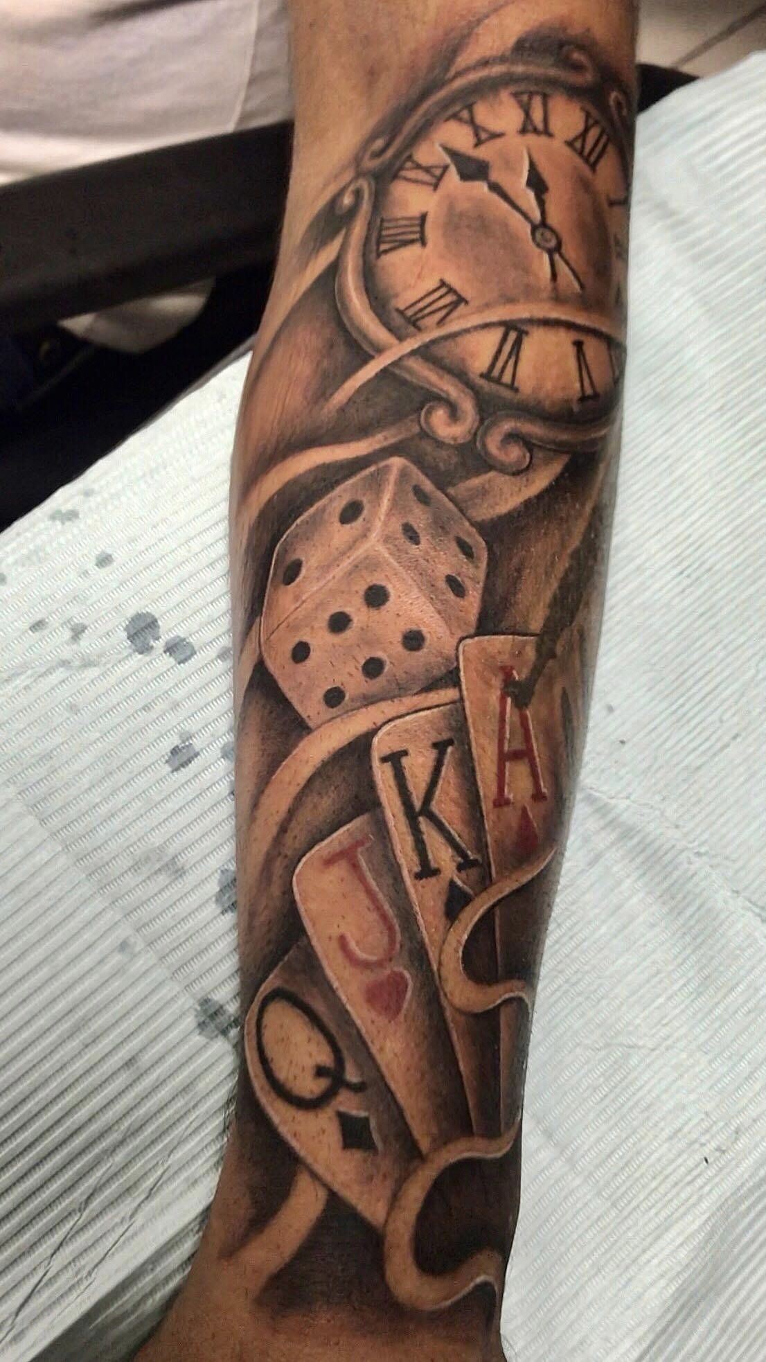 A man has a tattoo of dice playing cards and a clock on his arm
