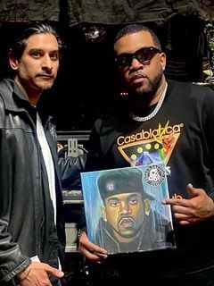 Two men are standing next to each other holding a painting of a man.