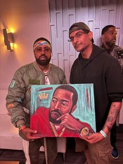 Two men are standing next to each other holding a painting of a man.
