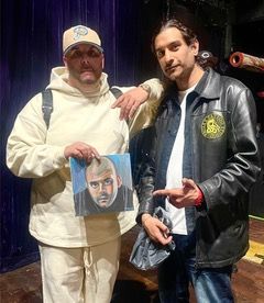 Two men are standing next to each other holding a painting of a man 's face.