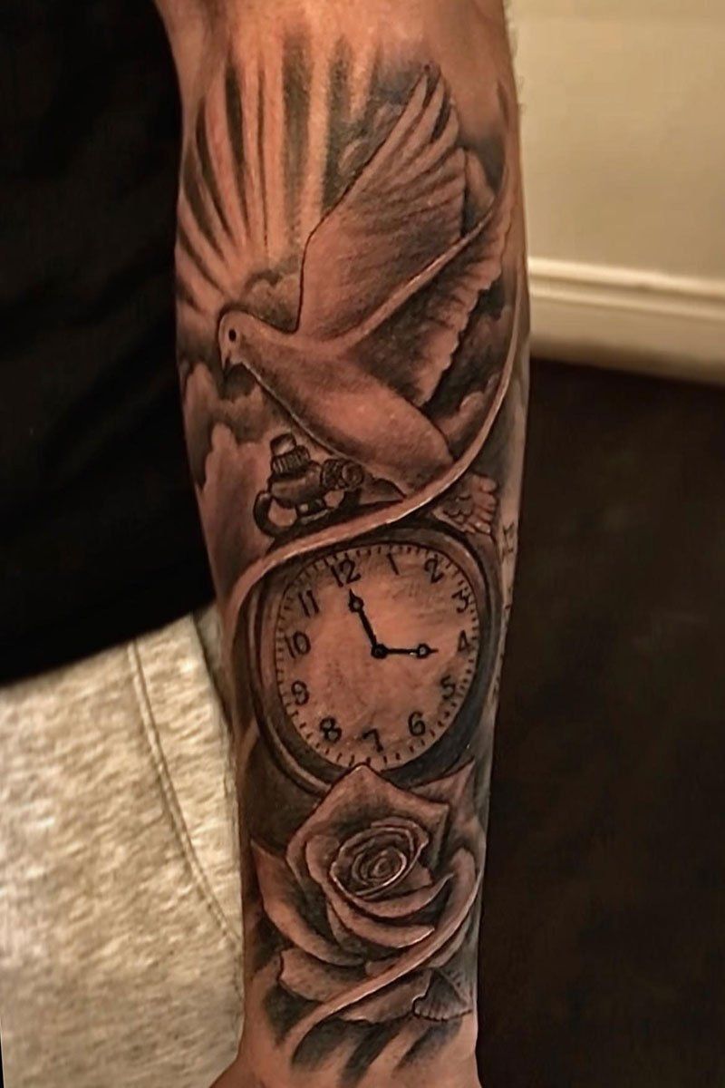 A man has a tattoo of a dove and a pocket watch on his forearm