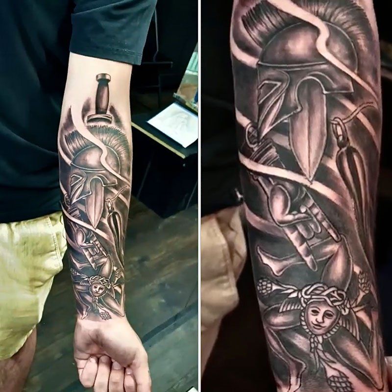 A man has a tattoo of a spartan helmet on his forearm.