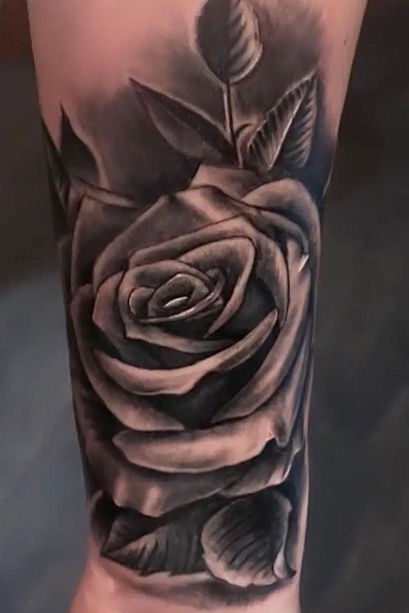 A black and white tattoo of a rose on a person 's arm.