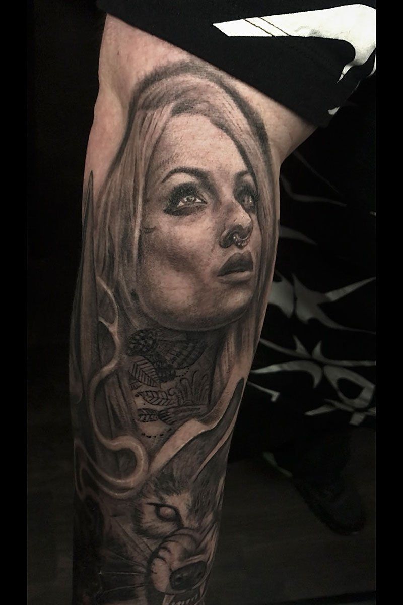 A black and white tattoo of a woman 's face on a leg