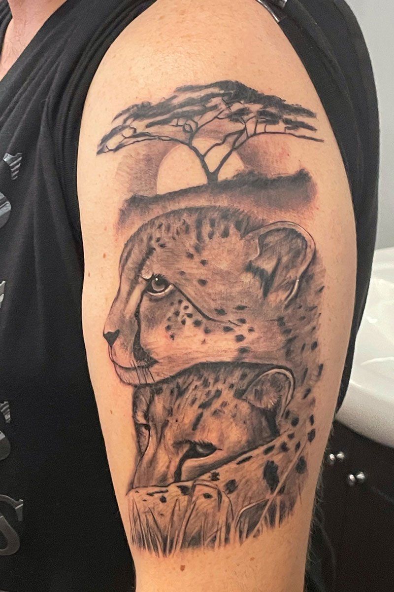 A person has a tattoo of a cheetah and a tree on their arm