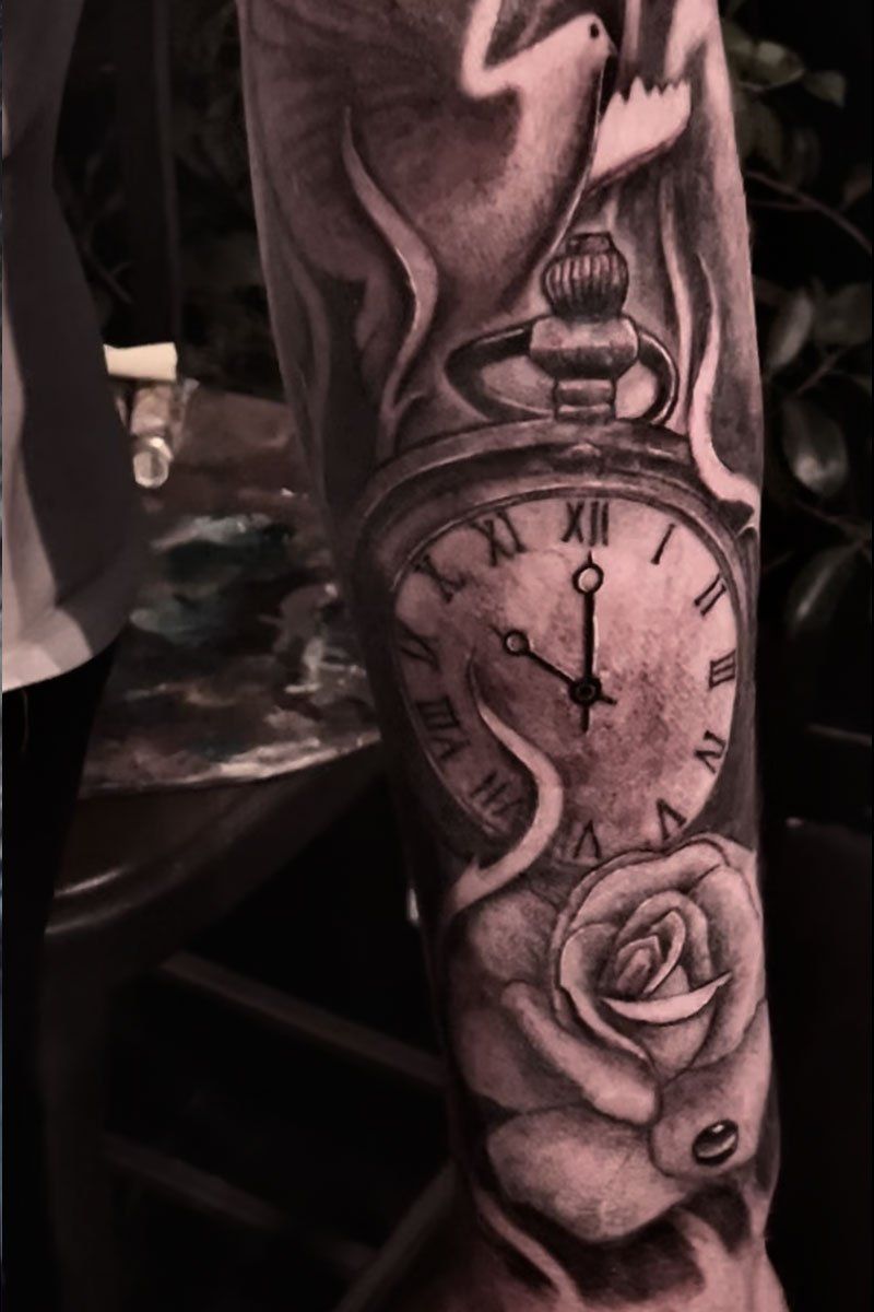 A man has a tattoo of a pocket watch and a rose on his arm