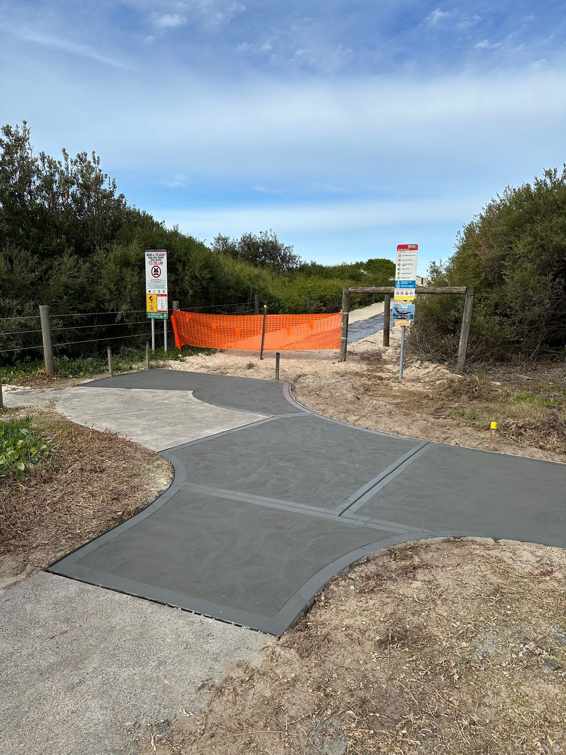 A concrete walkway leading to a beach with a fence in the background.