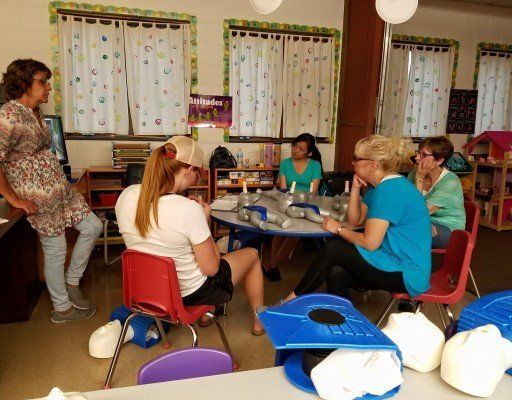 A group of women are sitting around a table in a classroom