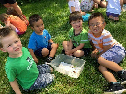 A group of young boys are sitting on the grass with a plastic container.