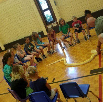 A group of children are sitting around a snake in a gym.