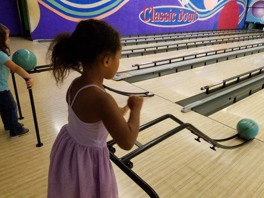A little girl in a pink dress is playing bowling