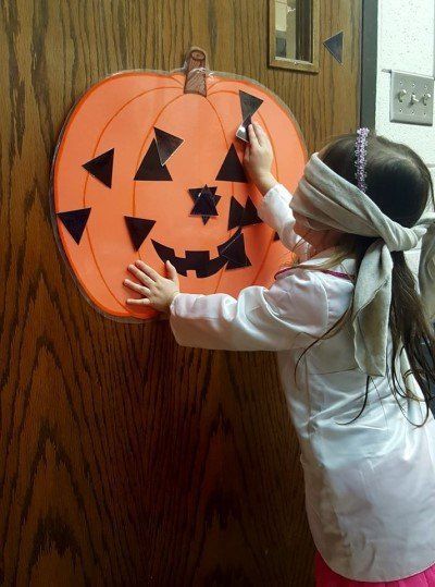 A little girl wearing a blindfold is painting a pumpkin on a wooden door