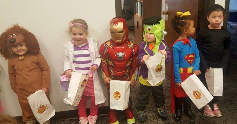 A group of children dressed in costumes are standing next to each other holding treat bags.