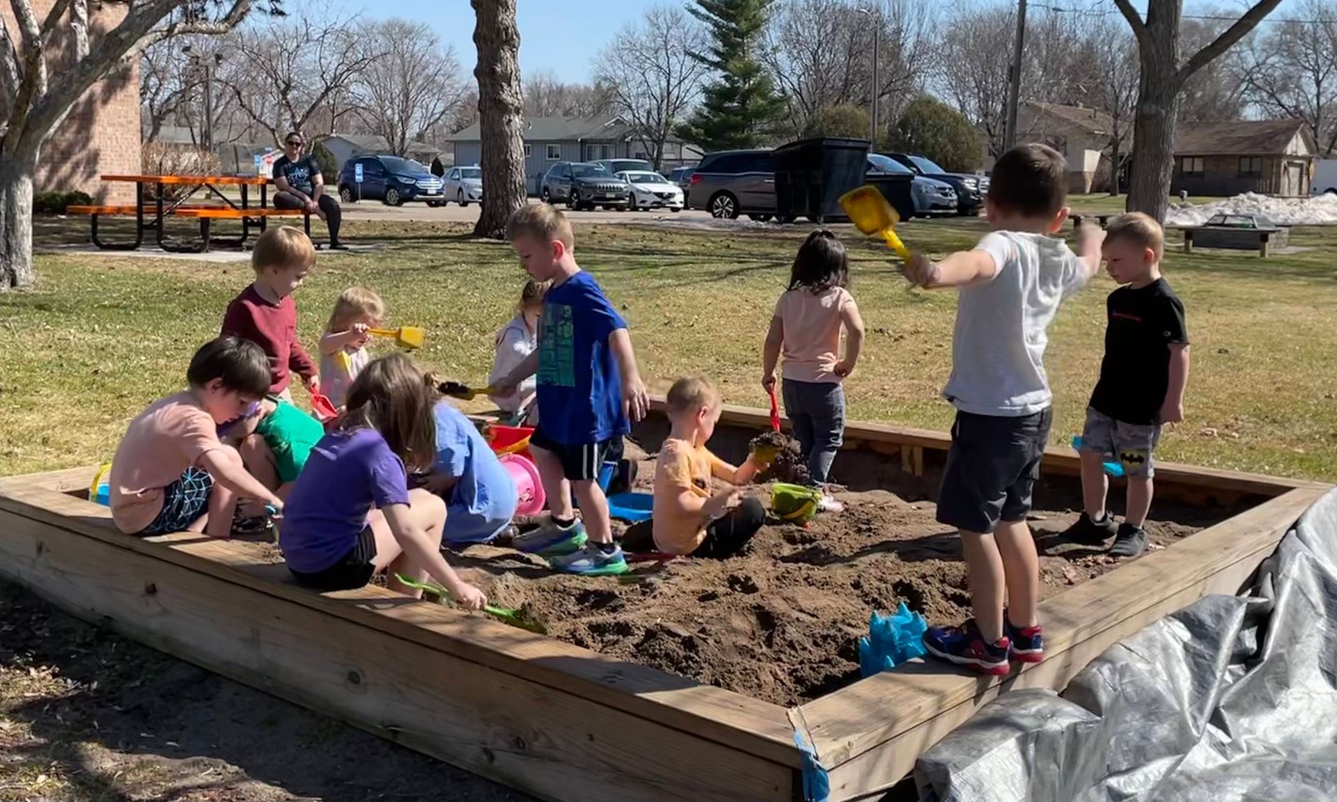 A group of children are playing in a sandbox in a park.