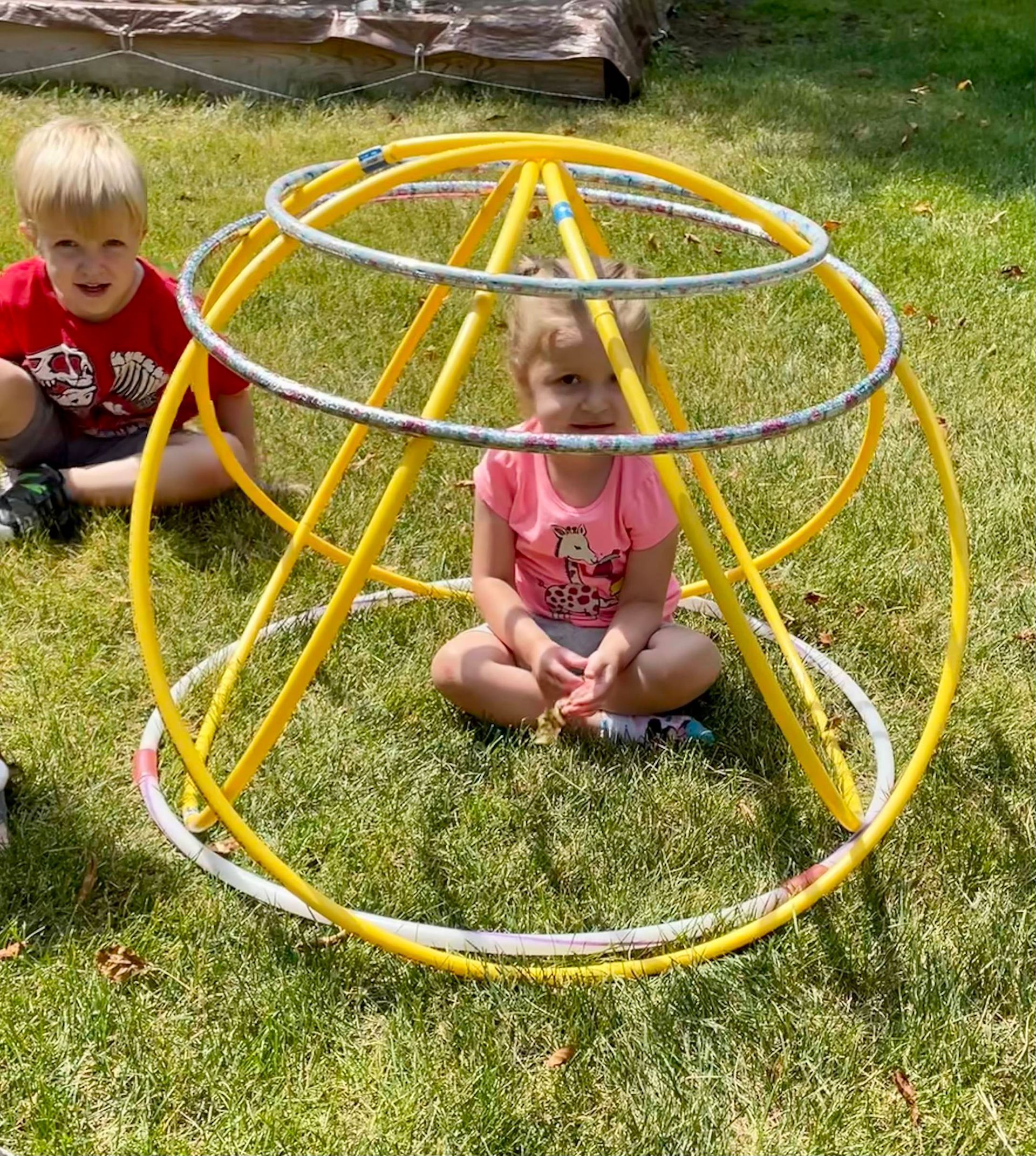 A boy and a girl are sitting in the grass next to a yellow hula hoop.