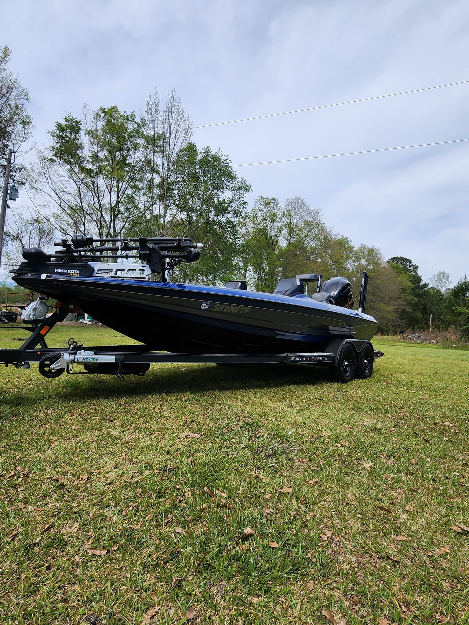 A Blue and Black Bass Boat Sits on a Trailer in a Grassy Field — Valentine Detailing LLC in Walterboro, SC