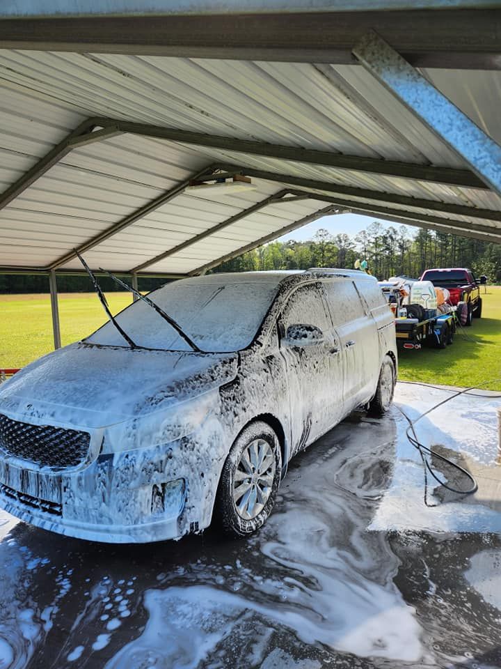 A Van Covered in Thick White Soap Suds Being Washed Under a Metal Carport — Valentine Detailing LLC in Walterboro, SC