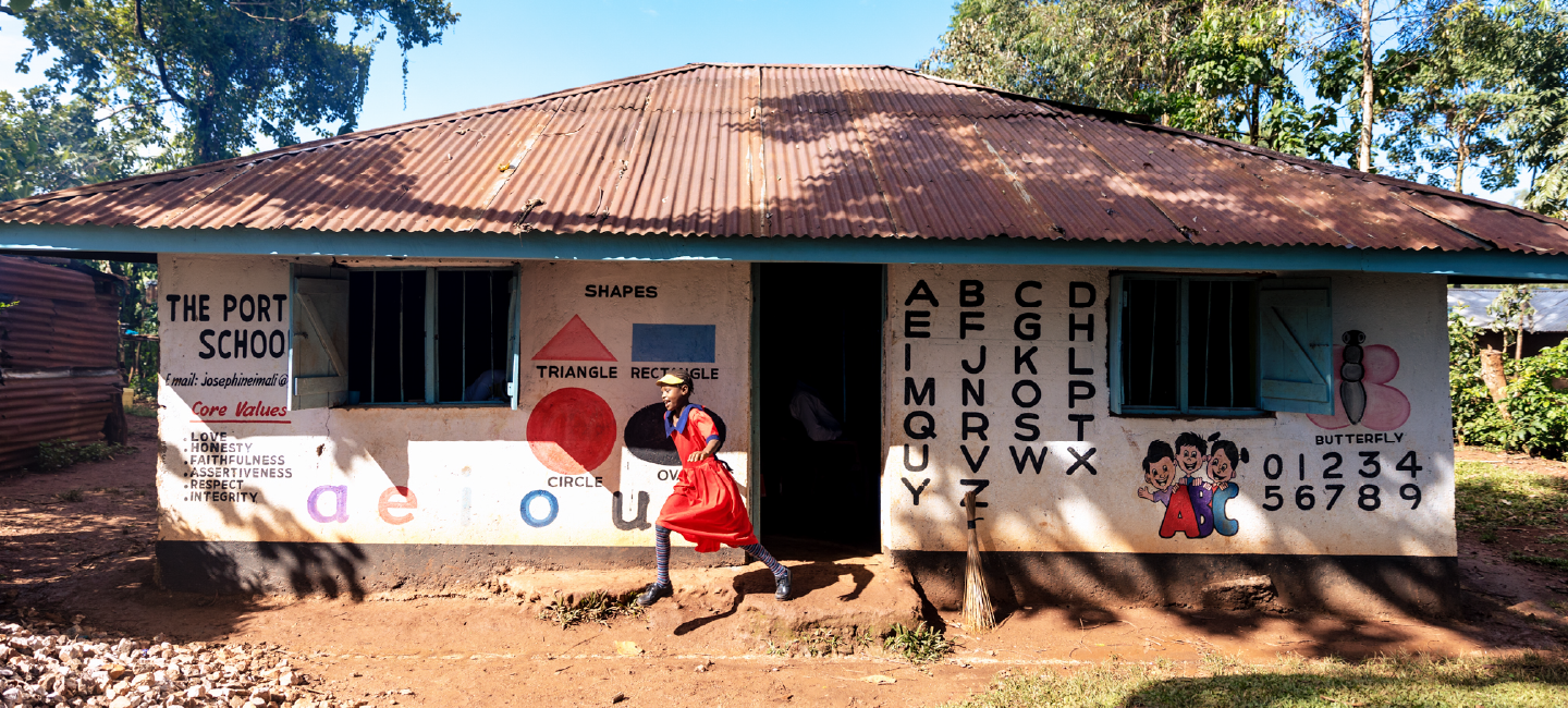 A child walking past her school building in Kenya, decorated with educational murals showing letters, numbers, and shapes.