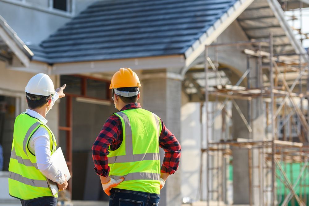 Two construction workers are standing in front of a house under construction.