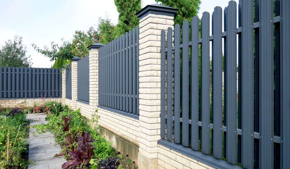 A black picket fence is surrounded by white brick pillars in a garden.