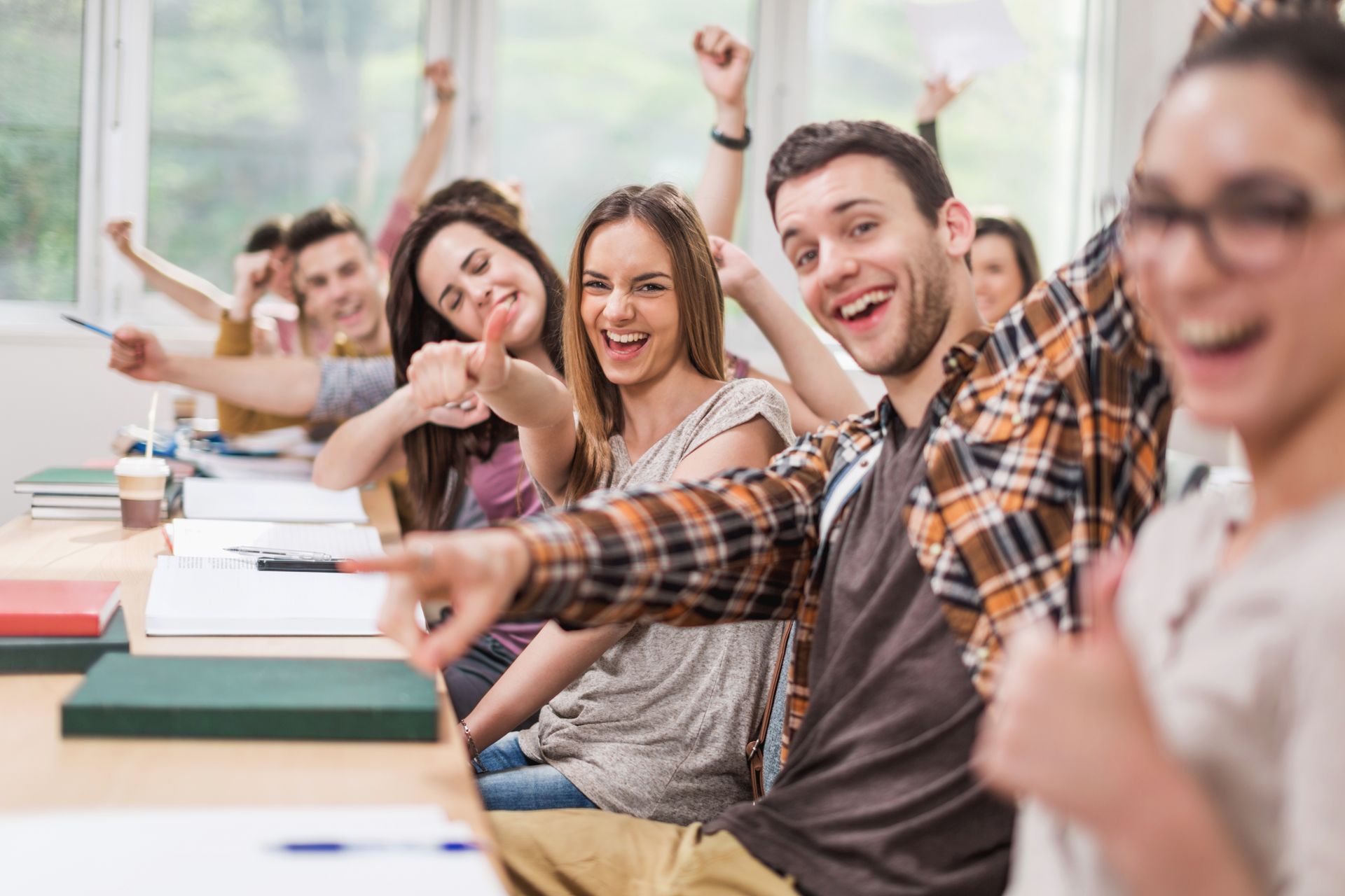 Studenti sorridenti in classe, che festeggiano con le braccia alzate e i pollici in su.