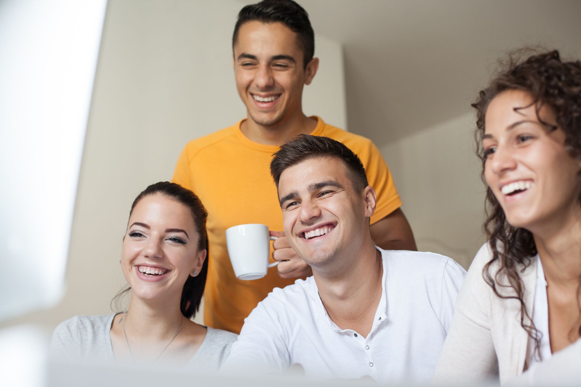 Quattro giovani adulti ridono mentre guardano lo schermo di un computer.