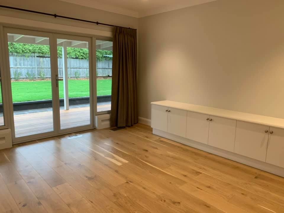 An Empty Living Room with Hardwood Floors and Sliding Glass Doors Leading to A Patio — GMT Builders Pty Ltd in Bowral, NSW