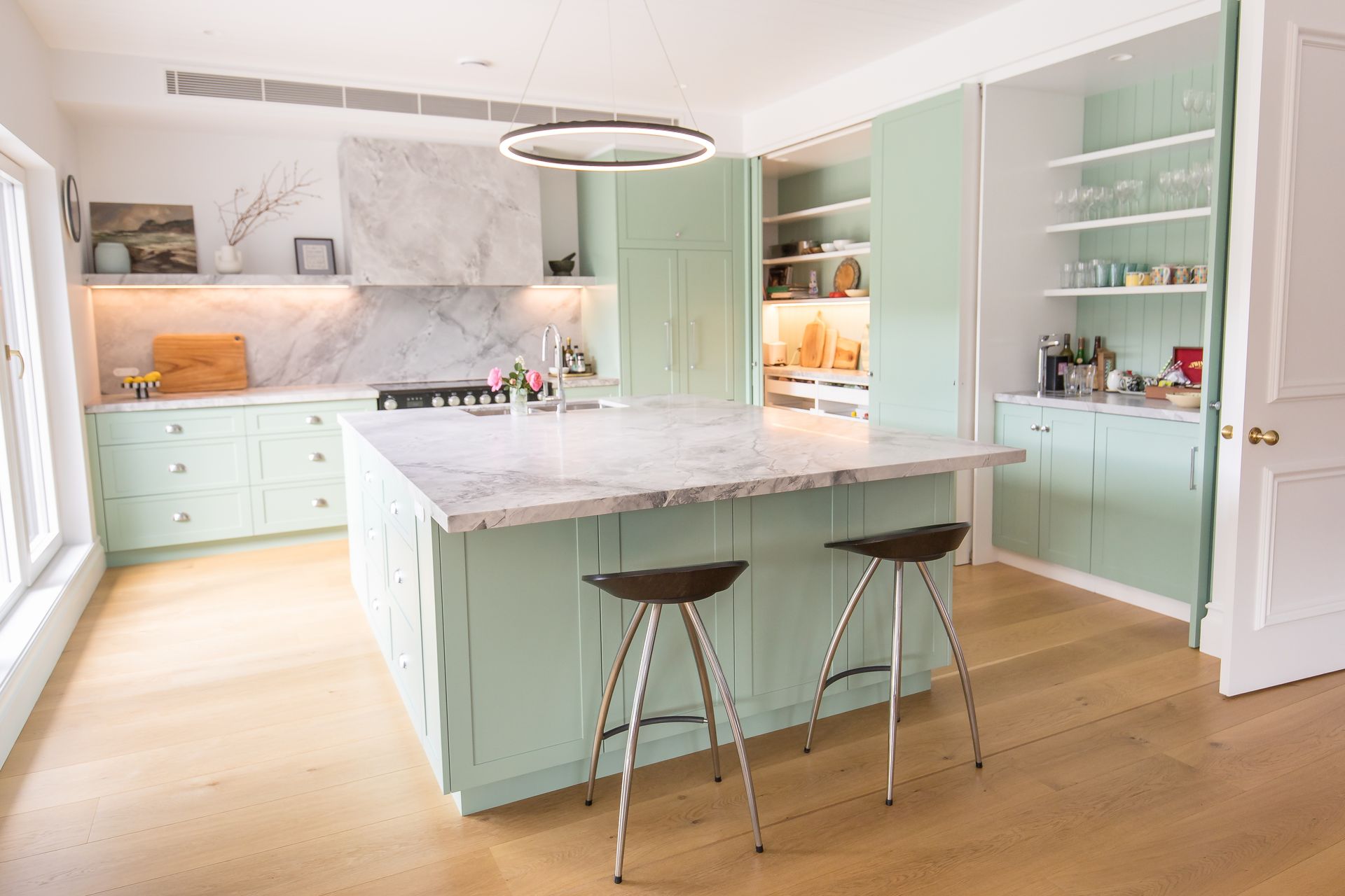 A Large Light Green Kitchen With An Island Bench And Two Black Stools — GMT Builders Pty Ltd in Nowra, NSW