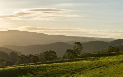 Sun is Shining Through the Clouds Over a Grassy Hillside With Mountains — GMT Builders Pty Ltd in Kangaloon, NSW