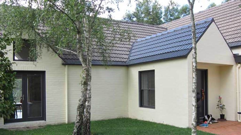 A white house with a blue roof and trees in front of it — GMT Builders Pty Ltd in Milton Park, NSW