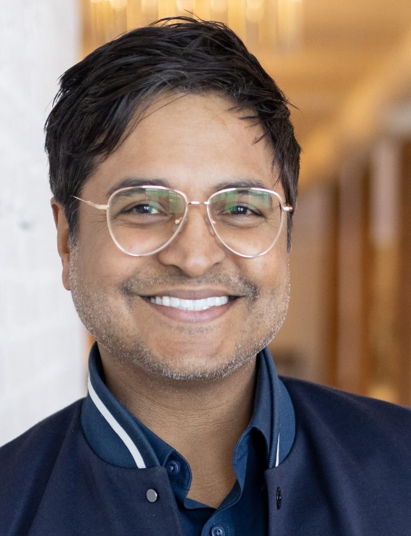 Bald man with brown eyes smiles brightly, looking directly at the viewer.