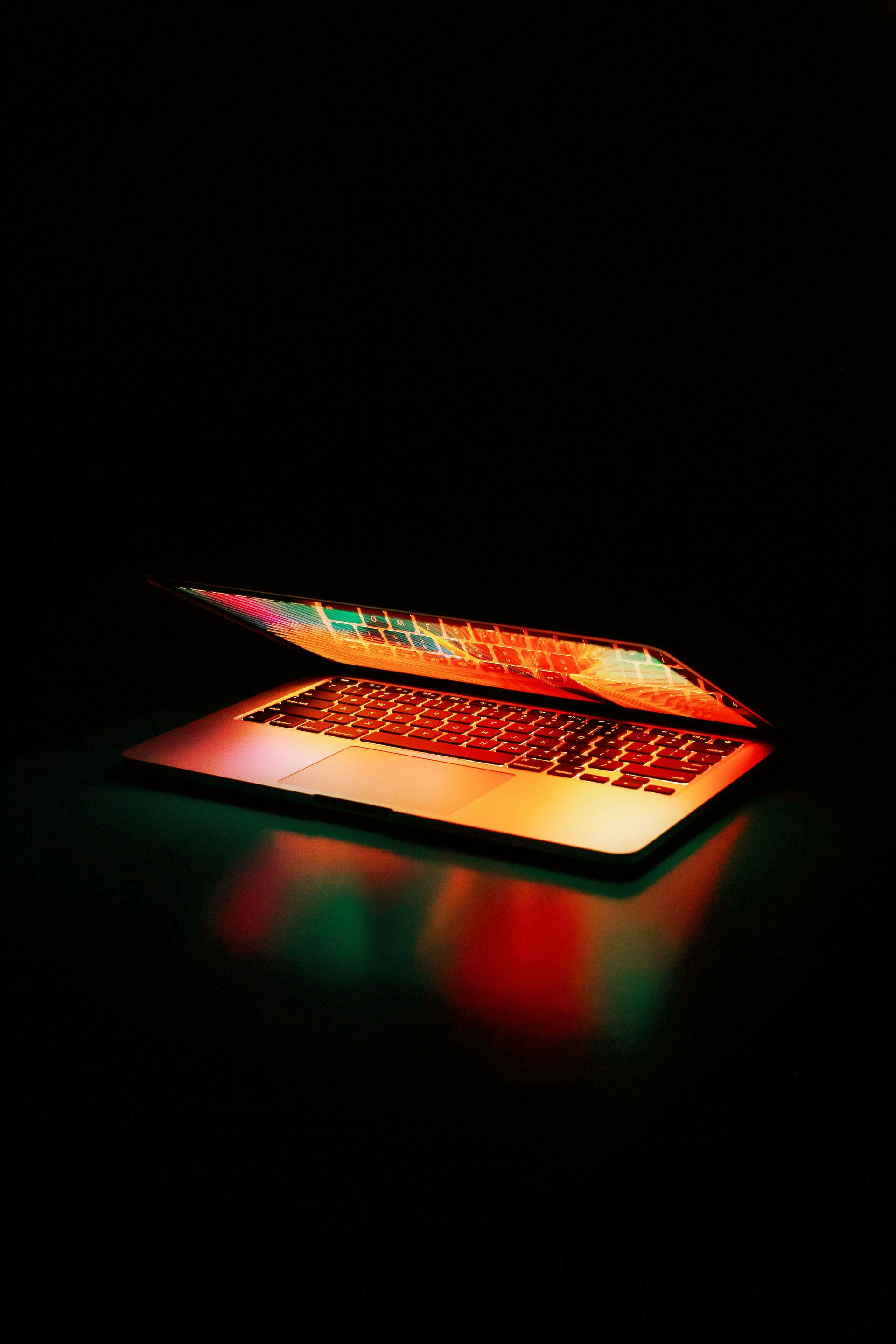 Lit-up laptop in the dark, glowing orange and green.
