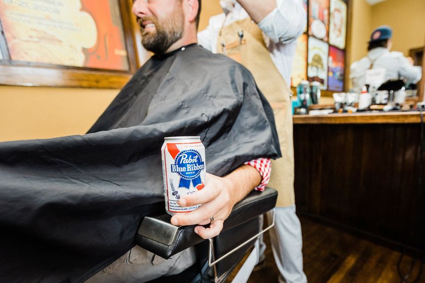 Man holding a beer while he gets his hair cut at the Start Barber Shop