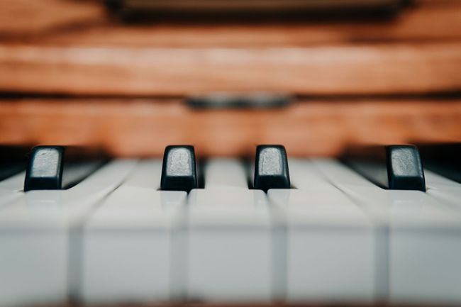 A horizontal shot of an wooden acoustic piano with with a focus on the piano keys.