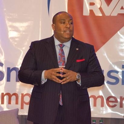 A man in a suit and tie stands in front of a sign that says rva